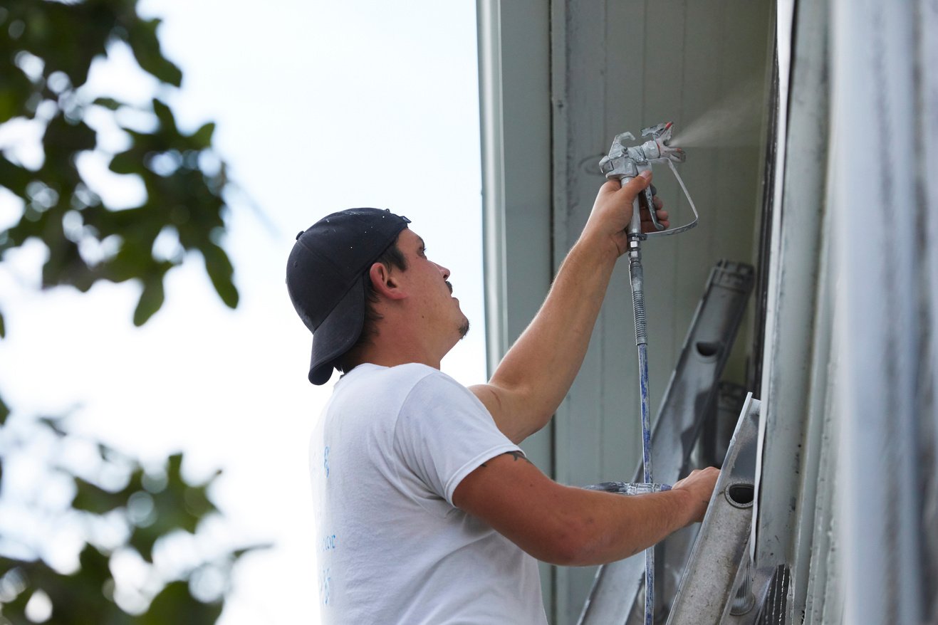 Man Spraying Paint On Exterior of Old Home